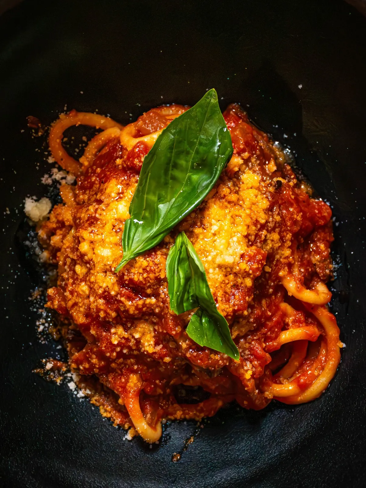 Pasta con salsa de tomate, queso rallado y dos hojas de albahaca, vista desde arriba.